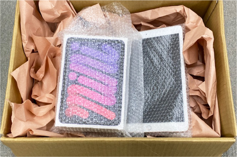 段ボール箱にipadを入れ、まわりに新聞紙など緩衝材を詰めている様子